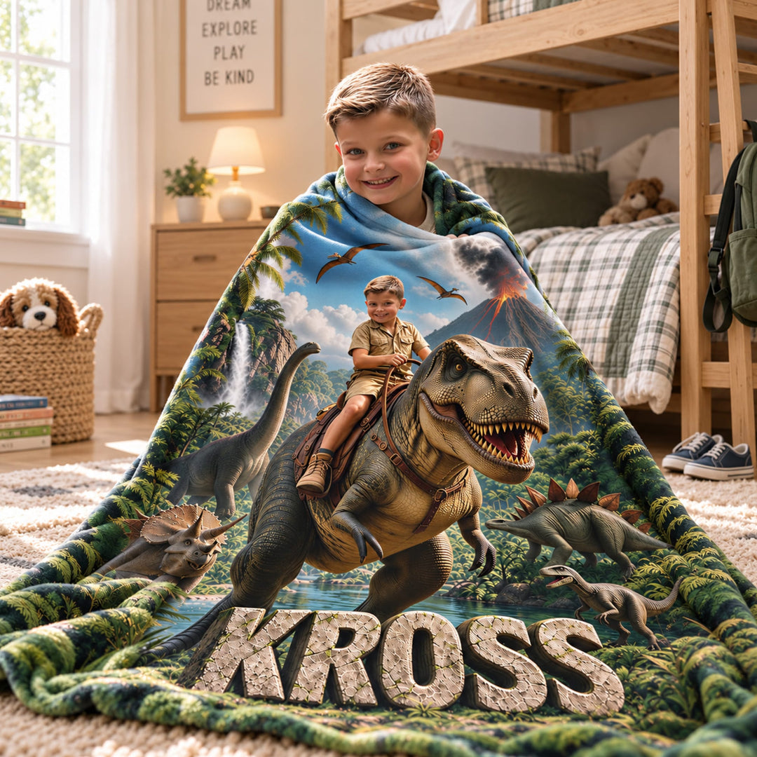 Boy wrapped in a personalized dinosaur blanket showing him riding a T. rex through a jungle, with his name carved in stone letters