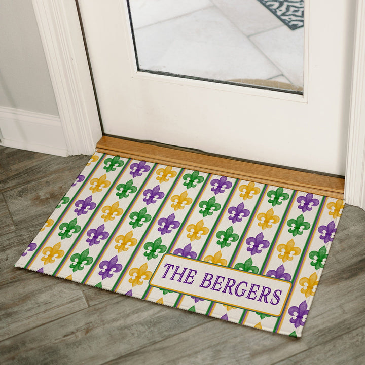 Personalized Mardi Gras fleur-de-lis welcome mat with purple, green, and gold stripes, customized with family name, placed at a kitchen entryway.