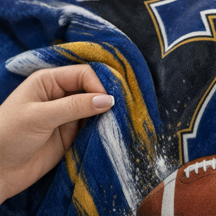 A hand pinching the soft minky fabric of the football blanket, showing the plush pile and crisp print. Printed and shipped from Louisiana.